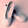 A pair of white ballet flats with light blue decorative stitching and bows, positioned on a pale pink background.