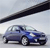 Blue sedan car with silver wheels positioned under a dark diagonal beam against a light gray background.