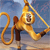 Golden monkey with brown accents stands on a pole, holding a rope looped around its body against a blue sky background.
