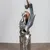 Pixelated figure in dark clothing holding a raised object against a light background with a brown floor line.