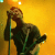 Pixelated image of a person holding a microphone against a yellow background with light effects.