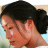 Pixelated close-up of a person with dark hair tied in a bun, showing side profile from shoulder to top of head against light background.