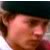 Pixelated close-up of a person's face with light skin tone, dark hair, and a neutral expression against a dark background.