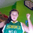 Pixelated image of a person in a green and white sports jersey with visible text, holding a blue object against a green background.