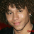 Pixelated close-up of a person with short dark hair, light skin, and a thin dark necklace against a dark background with red accents.
