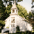 Pixelated static image of a white building with a tower, surrounded by green foliage under a light sky.