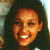 Pixelated static image of a person with dark hair and warm-toned skin, smiling broadly with visible teeth against a blurred background.