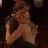 A pixelated figure in a dark setting with light-colored clothing, holding an object near the face.