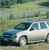 Pixelated image of a white sedan with blue accents parked on a grassy field with blurred green background.