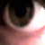 Pixelated close-up of a human eye with visible iris and pupil, showing partial eyelid structure against dark background.