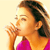 A pixelated close-up of a person with brown hair wearing a pink top, blowing a kiss with their right hand near their mouth against a light background.