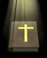 A brown book with a yellow cross on its cover under a spotlight, shown in two slightly different views.