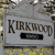 A static pixelated image shows a gray rectangular sign with the word "KURKUOP" in bold brown letters and a black rectangular bar below it, set against a blurred background of yellow and brown tones.