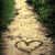 A pixelated image shows a sandy hill with two heart shapes carved into it, surrounded by greenery and colorful radial lines.