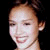 Pixelated close-up of a person's face with light skin tone, dark hair pulled back, and a neutral expression against a black background.
