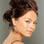 Pixelated close-up of a person with dark brown hair styled in a high bun, light skin tone, and pink lips, set against a solid gray background.