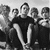 Black-and-white pixelated image of five people standing in a group, likely band members, with varying hairstyles and clothing styles visible at low resolution.