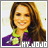 Static pixelated image of a person with long brown hair wearing a purple jacket over a green shirt, with visible text at the bottom right corner.