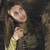 Pixelated image of a person with long brown hair wearing a green top, holding a hand near their face against a dark background.