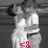 Pixelated grayscale image of a figure with a white top and dark hair, holding a red and white object near the lower body.
