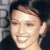 Pixelated close-up of a smiling person with short dark hair, wearing a dark top against a blurred background.