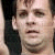A pixelated close-up of a person holding a dark object near their face, with visible skin tones and partial facial features.