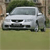 A silver sedan with a dark grille and headlights is positioned on a grassy area with trees in the background.