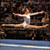 A pixelated gymnast in a white leotard performs a split on a balance beam against a dark background with blue and brown tones.