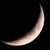 A crescent moon shape rendered in pixelated light brown and white tones against a solid black background with faint blue speckles.