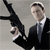 A pixelated figure in a black suit holds a large black rifle with both hands, positioned horizontally in front of the body against a plain gray background.