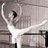 Pixelated grayscale image of a figure in ballet pose with arms extended and one leg lifted, set against abstract background shapes.