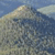 Pixelated static image of a mountain peak with blue sky and clouds, rendered in low-resolution with muted earth tones and blue hues.