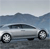 Pixelated silver sedan with black wheels on a road, mountains in background, blue sky above.