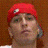 Pixelated static image of a person wearing red headwear with a white emblem, set against a brown background.