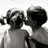 Two pixelated figures in grayscale, one with braided hair and the other with short hair, facing each other closely against a white background.
