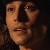 Pixelated close-up of a person's face with neutral expression, dark background, and visible clothing texture.