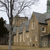 Pixelated static image of a stone building with multiple windows, a tree with bare branches, and a light sky background.