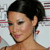 Pixelated close-up of a person with short dark hair, light skin, and a neutral expression, wearing a thin necklace and small earrings against a blurred background.