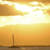 A static pixelated image depicts a sunset over water with a single sailboat silhouette against warm orange and yellow gradients.