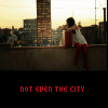 A static image of a girl in a white top and red pants leaning on a rooftop railing with a cityscape background, overlaid with changing text.