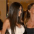 Two figures in close physical proximity, one with long dark hair wearing a white sleeveless top, the other with short light hair in a dark top, against a warm-toned background.