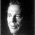 Black-and-white pixelated static image of a human face with visible facial features and grayscale shading on a dark background.