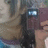 A pixelated image of a person with light brown hair holding a dark red device displaying two white rectangular shapes, wearing a blue and purple garment.
