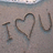 Static pixel art displays 'I' followed by a heart symbol and 'U' on a textured gray background with subtle blue and brown tones.