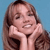 A person with light brown hair holds both hands near their face against a solid light blue background.