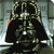 Pixelated static image of a dark figure in black armor with metallic silver accents and glowing white highlights, set against a blurred background.