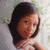 Pixelated image of a person with dark hair and light skin, wearing a white top against a blurred background.