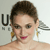 A pixelated close-up of a person with short brown hair, wearing gold earrings and red lipstick, against a light background with partial dark text.