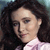 Pixelated close-up of a person with dark curly hair wearing a light pink collared shirt against a blurred background.