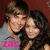 Two people pose closely together against a dark red background, with one person wearing a gray shirt and the other having long dark hair; pink text 'ZAC' appears at bottom left.
